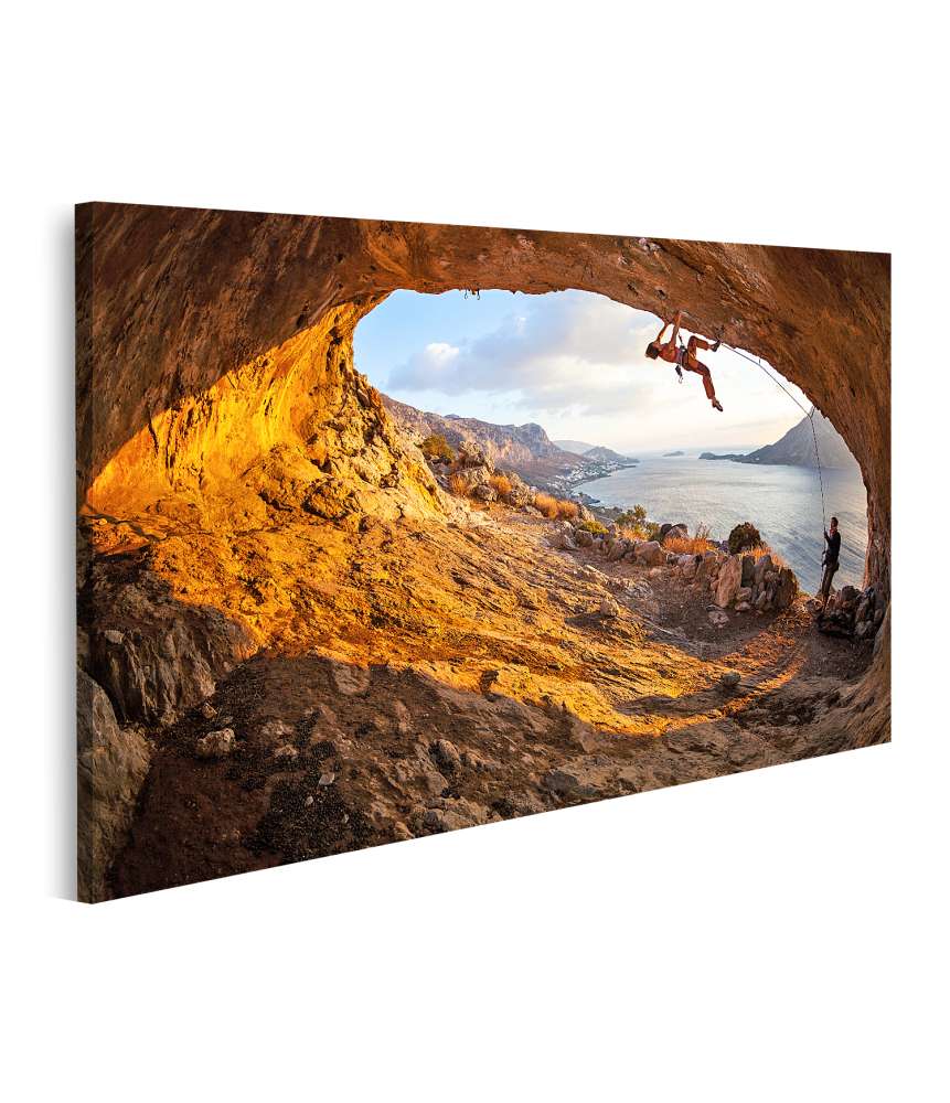 Bild auf Leinwand Junge Frau klettert in Höhle mit atemberaubender Aussicht im Hintergrund