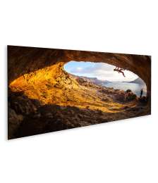 Bild auf Leinwand Junge Frau klettert in Höhle mit atemberaubender Aussicht im Hintergrund